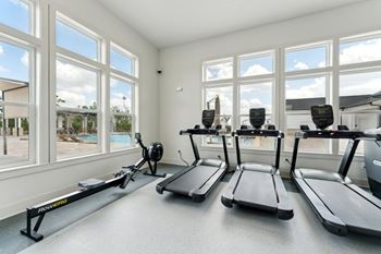 A room with treadmills and a view of the outdoors through the windows.